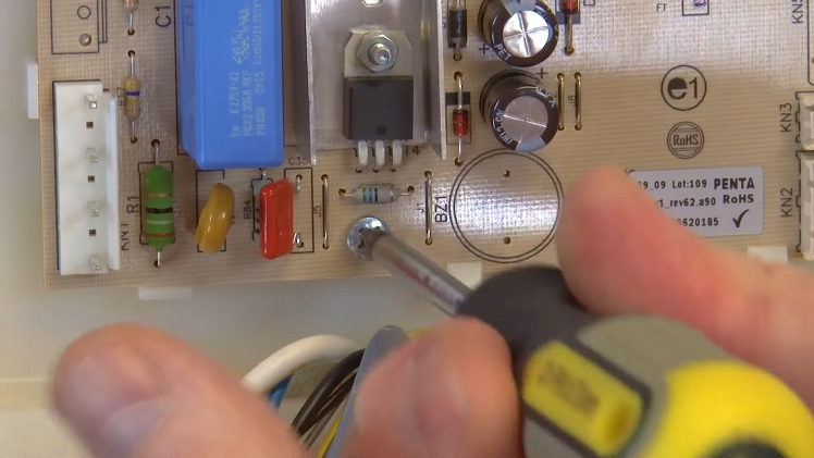 Using A Phillips Screwdriver To Remove The Screw That Holds The Main Fridge PCB In Place