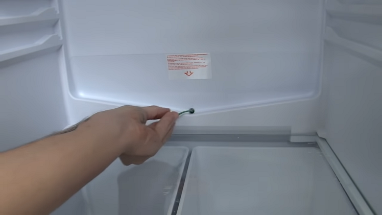 Using A Fridge Drain Hole Cleaning Tool To Unblock Any Food Or Debris Clogging Up The Drain Hole
