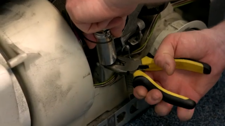 Using A Pair Of Pliers To Unscrew The Nut Underneath The Capacitor That Holds It In Place