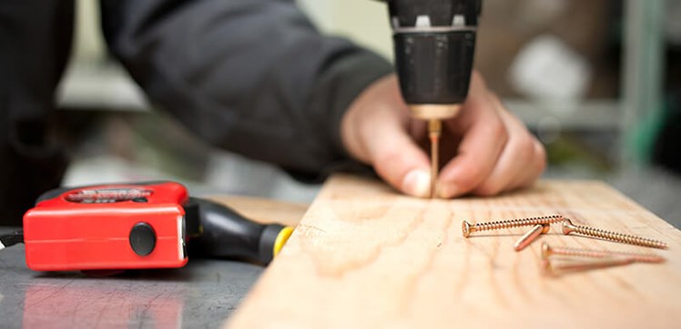 Screwing a screw through some wood with an electric drill