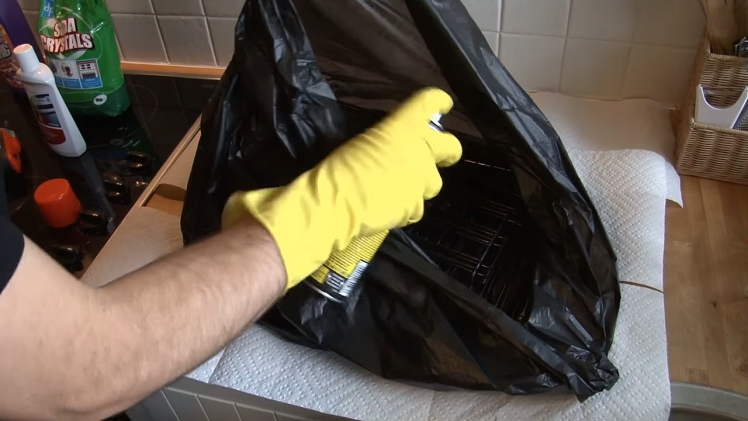 Using A Oven Cleaner Spray To Clean The Oven Shelves Inside A Black Bin Liner