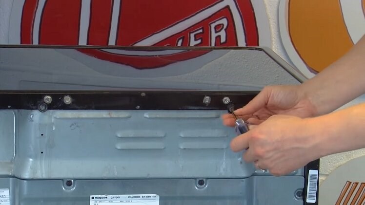 Unscrew the two screws at the back of the oven that hold the top panel in place