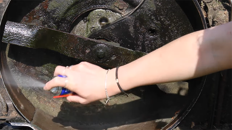 Spraying Any Bare Metal Areas With WD-40 To Help Protect The Petrol Lawnmower From Rust And Corrosion