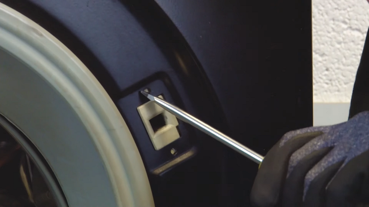 Press the screwdriver blade into the two door lock lugs from the outside of the machine.