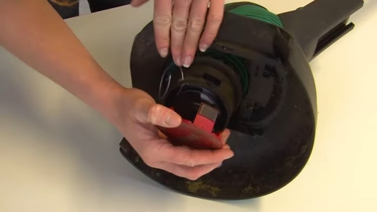 Removing The Spool Cover By Pressing In The Two Tabs On Either Side Of The Cover That Are Connected To The Trimmer Head