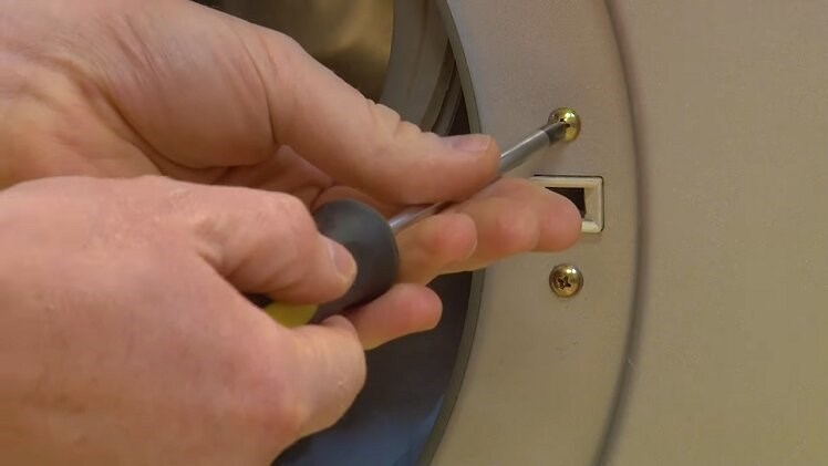 Use a Phillips screwdriver to unscrew the two screws that hold the door lock in place from the outside of the door frame