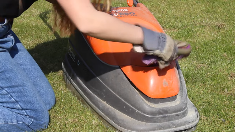 Using A Stiff Dry Brush To Scrub Away Dirt And Grass From The Lawnmower's Exterior And Housing Cover