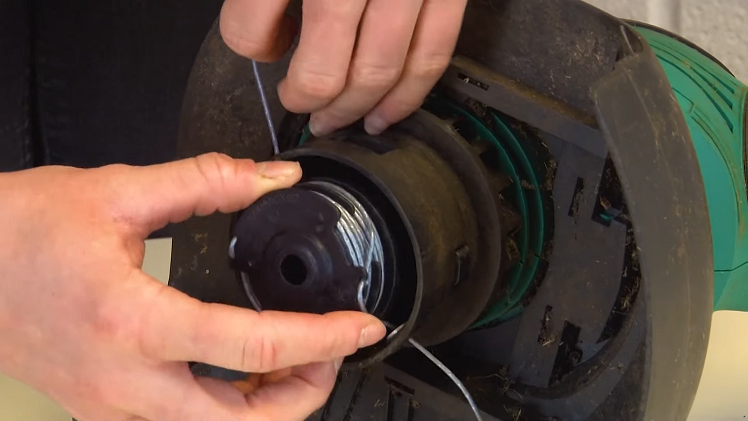 Feeding The Excess Line Through The Trimmer Head Outlet Holes And Pushing The Spool Onto The Spindle