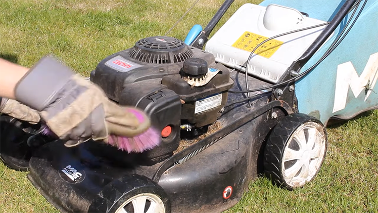Using A Stiff Dry Brush To Scrub Away Dirt And Grass From The Petrol Lawnmower's Body