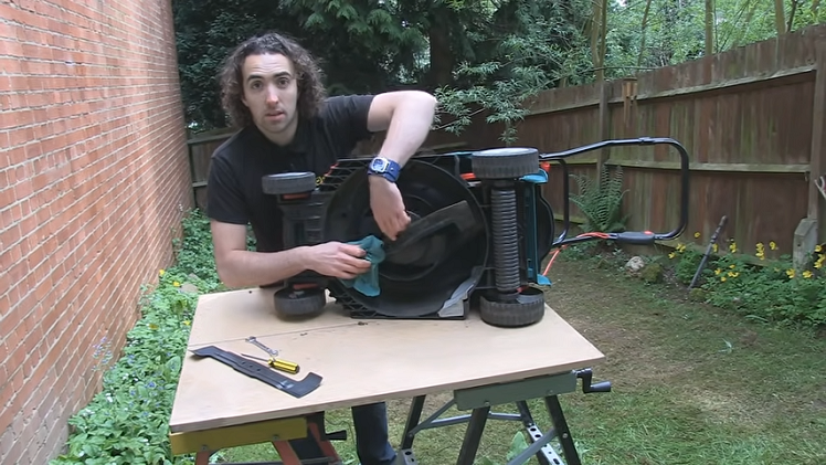 Holding The Lawnmower Blade In Place With A Cloth While Unscrewing The Central Locking Nut By Hand