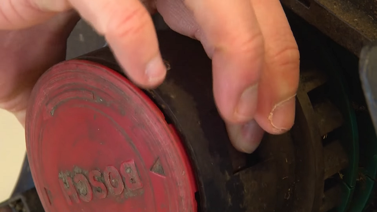 Pressing The Two Tabs Which Connect The Spool Cover To The Trimmer Head At The Same Time And Pulling The Cover Away And Lifting It Off Of The Spool