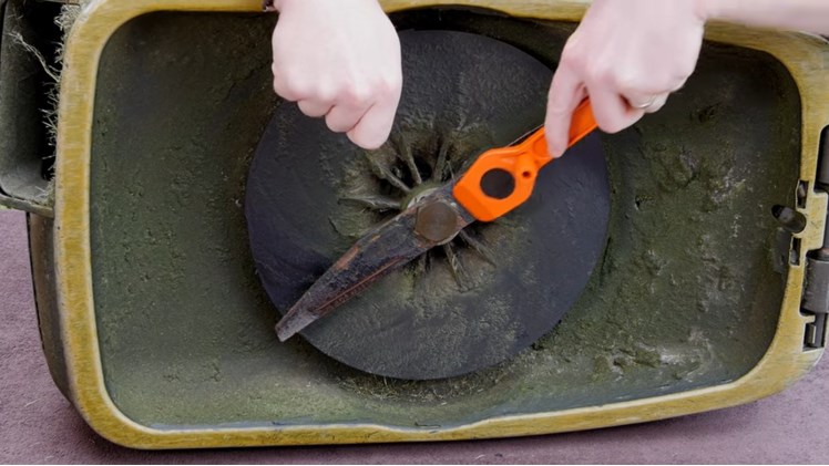 Using A Flymo Spanner To Scrape Any Debris Or Build Up From The Lawnmower Blade
