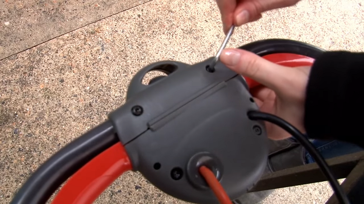 Using A Torx Head Screwdriver To Unscrew The Two Screws At The Top Of The Lawnmower Switch Box