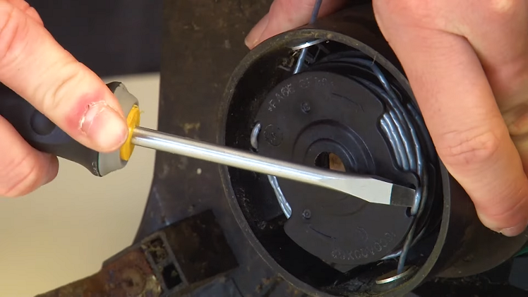 Using The Tip Of A Screwdriver And Pushing The Line Off The Spool Hooks