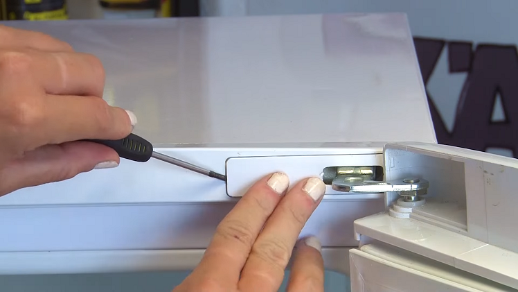 Inserting A Small Flat Blade Screwdriver Into The Far Side Of The Fridge Top Door Hinge Cover